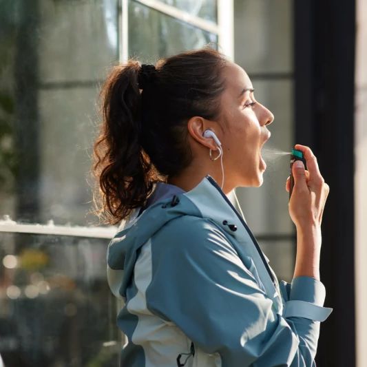 Une Femme utilisant la Vaporisateur buccal à la nicotine NICORETTE VapoÉclair SmartTrackMC dans sa bouche