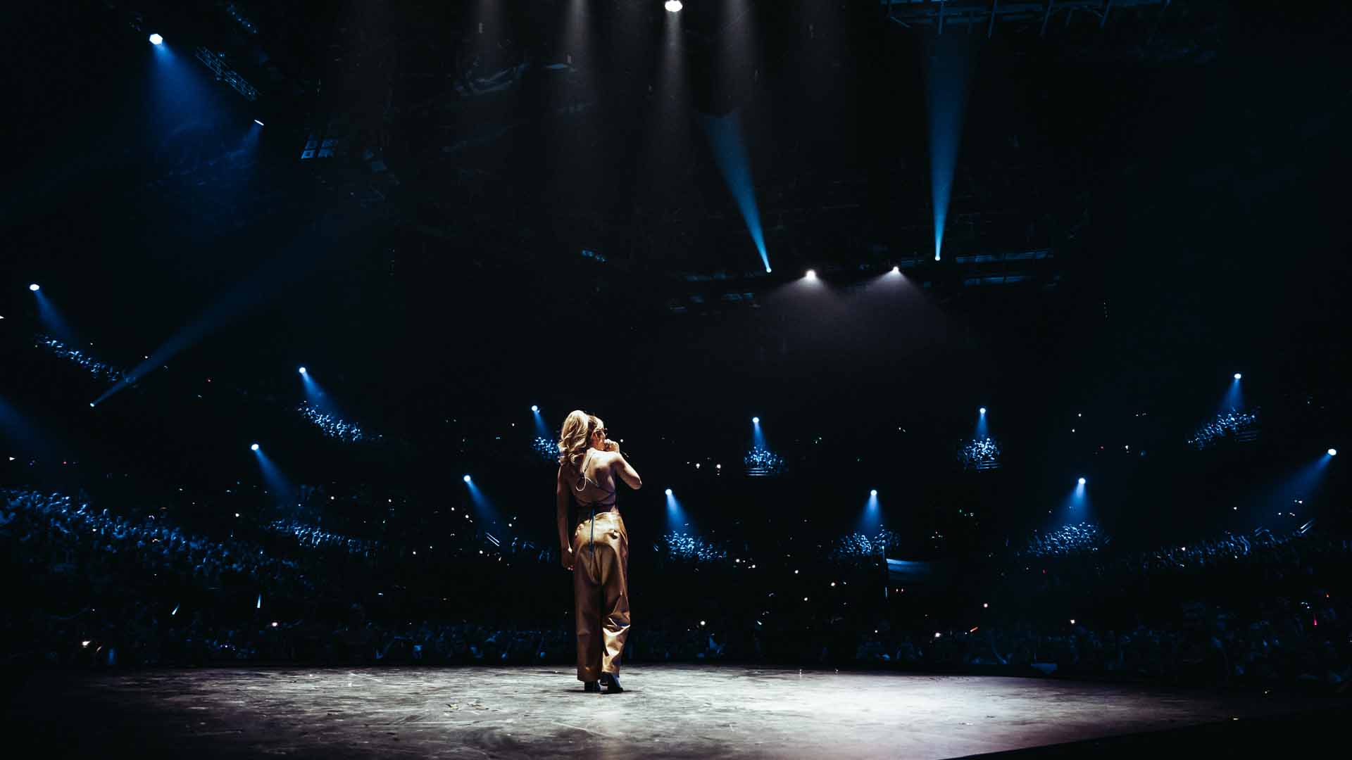 Anastacia performs at the AFAS Dome. The venue is dark. Only she is visible in the spotlight.