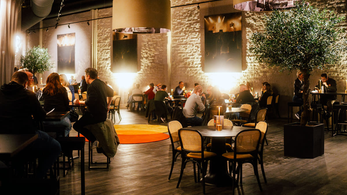 Bezoekers genieten van drankjes en gerechten in de sfeervolle Mastercard Lounge van de AFAS Dome, met warme verlichting, comfortabele zitplaatsen en een rustige loungesfeer voor de show.