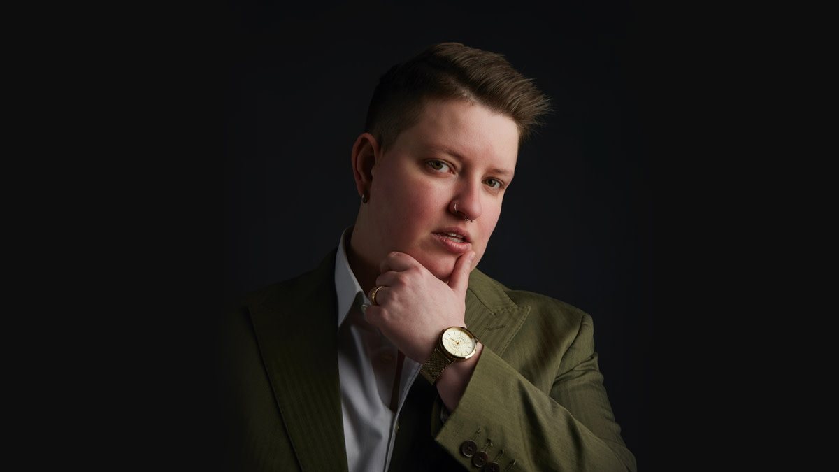 Ella Taylor in pak posteert voor de camera tegen een zwarte achtergrond.