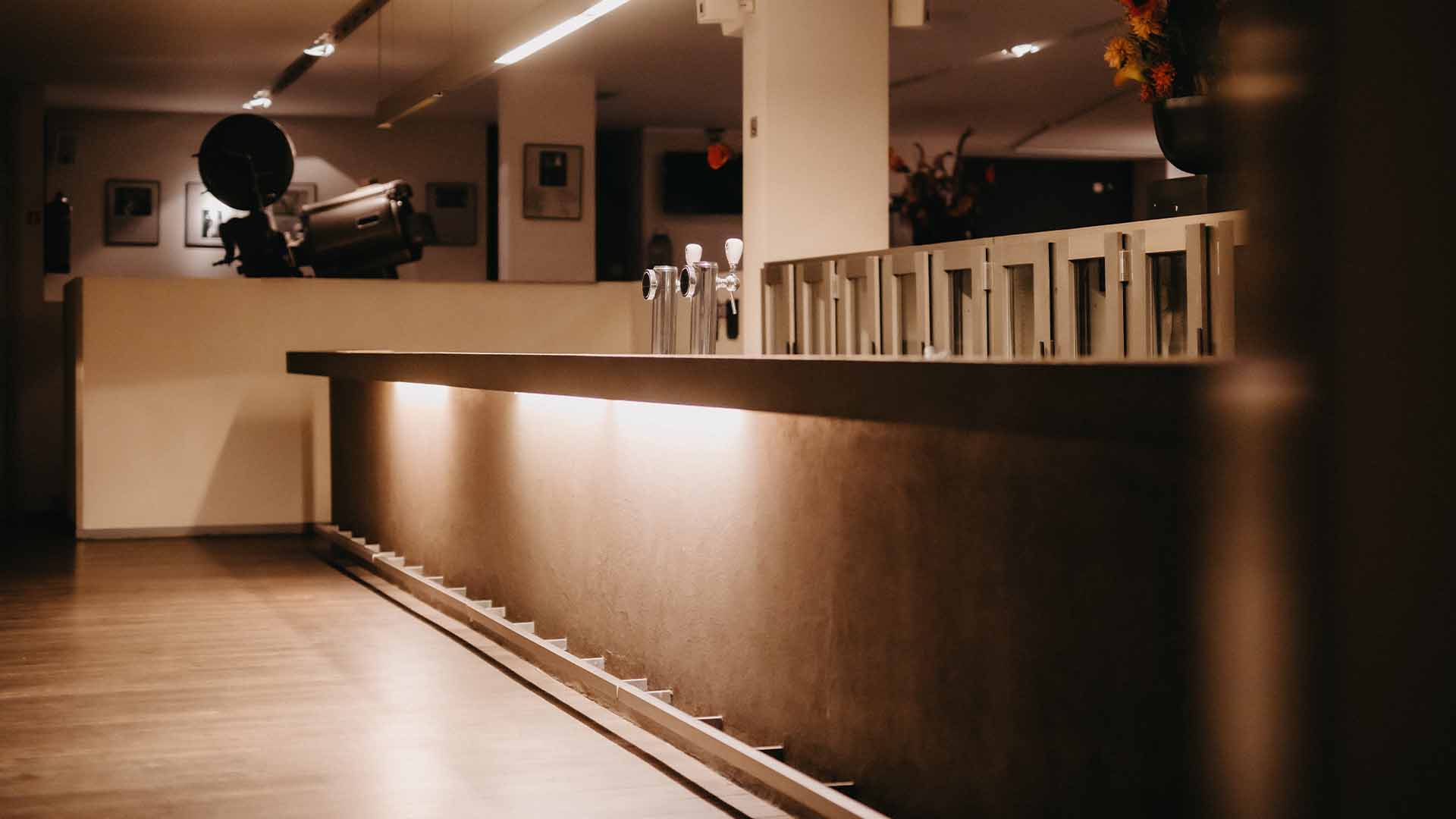 Een toog met twee tapkranen en enkele koelkasten naast elkaar. Op de achtergrond staat een oude filmprojector die verwijst naar het cinemaverleden van Capitole Gent.