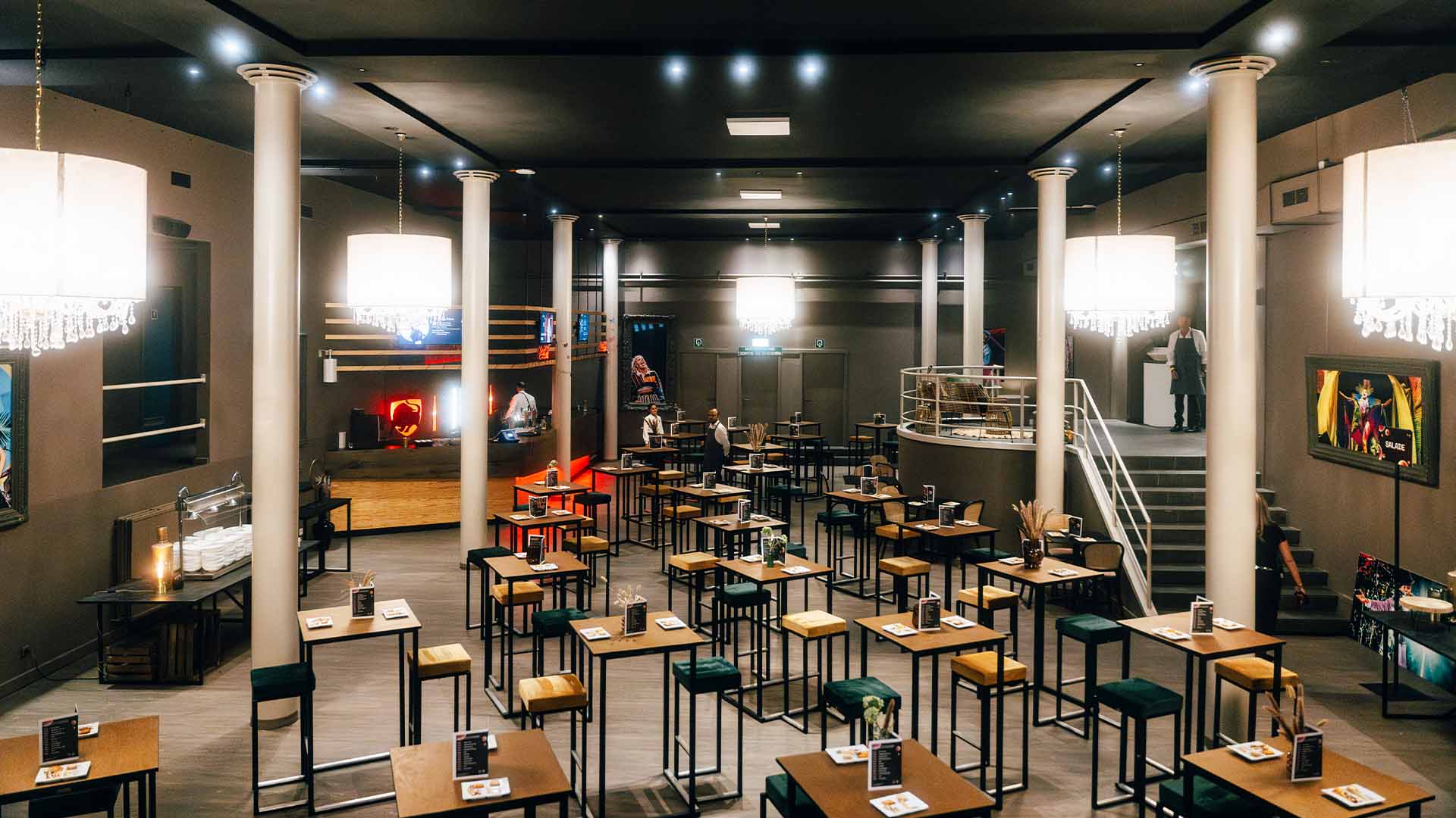 In de VIP Village staan verschillende hoge tafeltjes opgesteld. Links staat een buffettafel met stapels borden en achteraan is een bar. De zaal is leeg.