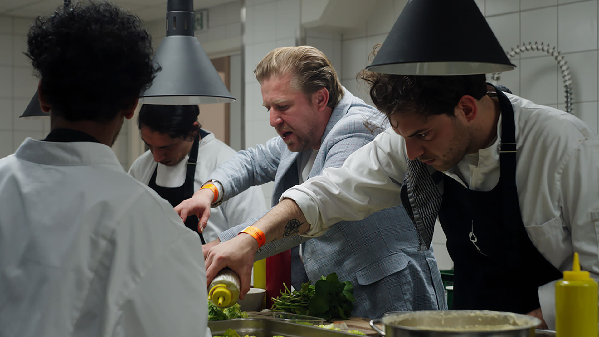 Chef Seppe Nobels in de keuken van de AFAS Lounge omringd door drie koks bezig met. het klaarmaken van een gastronomische maaltijd.