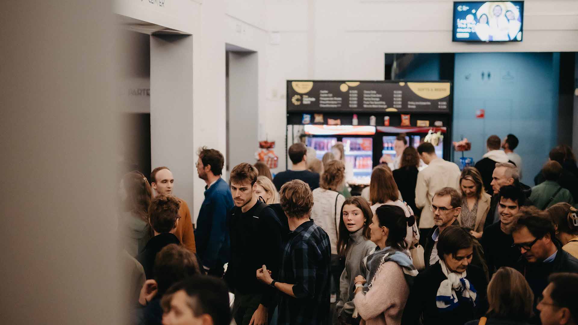 Een levendige menigte van bezoekers staat in de foyer van Capitole Gent, met op de achtergrond een bar.