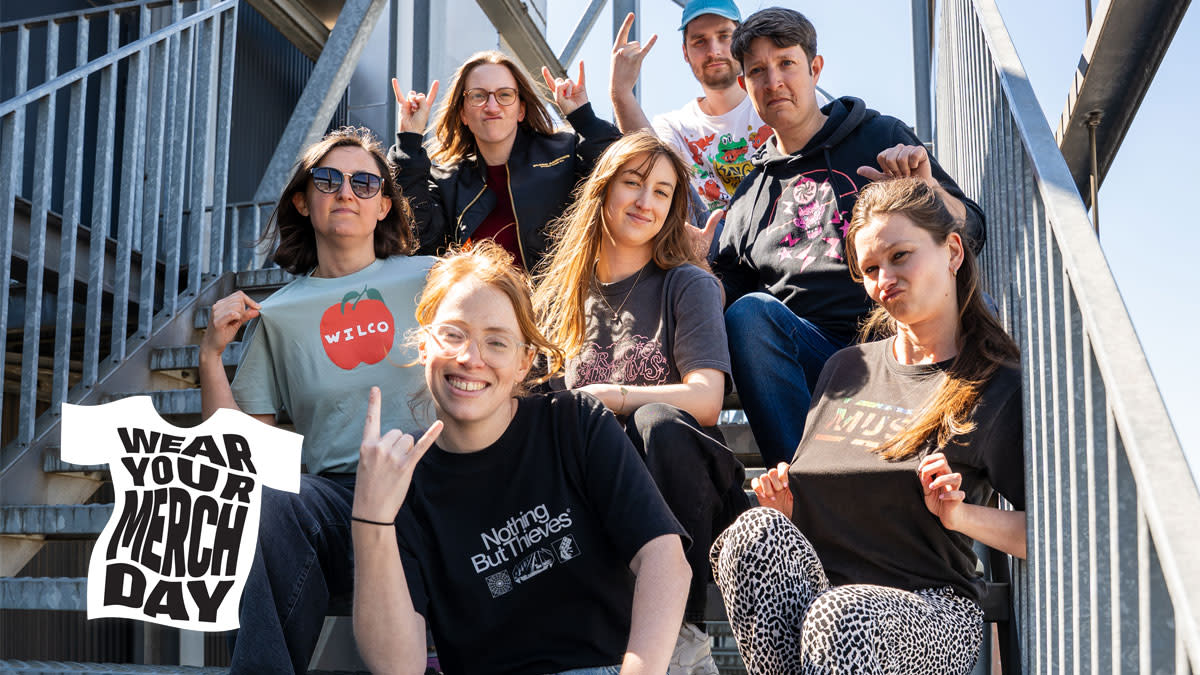 Un groupe de jeunes assis sur un escalier métallique, portant des t-shirts de groupes et posant de manière ludique pour le Wear Your Merch Day.