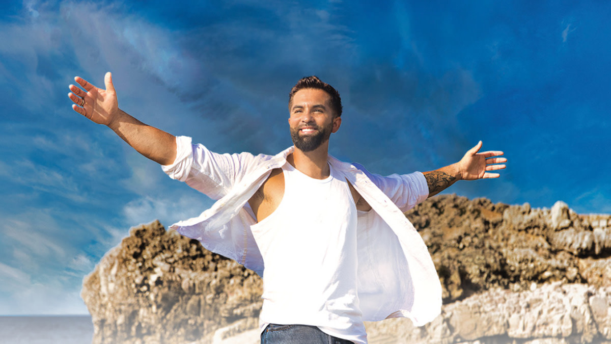 Kendji Girac staat met gespreide armen in een zonnig rotslandschap onder een felblauwe hemel