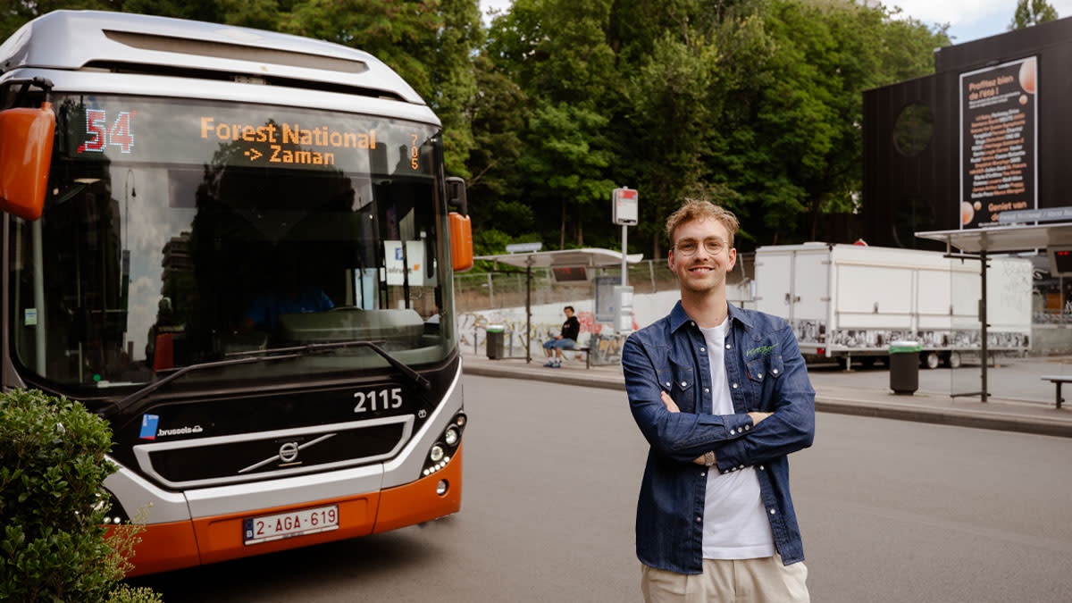 Léopold, Sustainability Assistent van Vorst Nationaal, staat lachend voor een bus met bestemming Vorst Nationaal.
