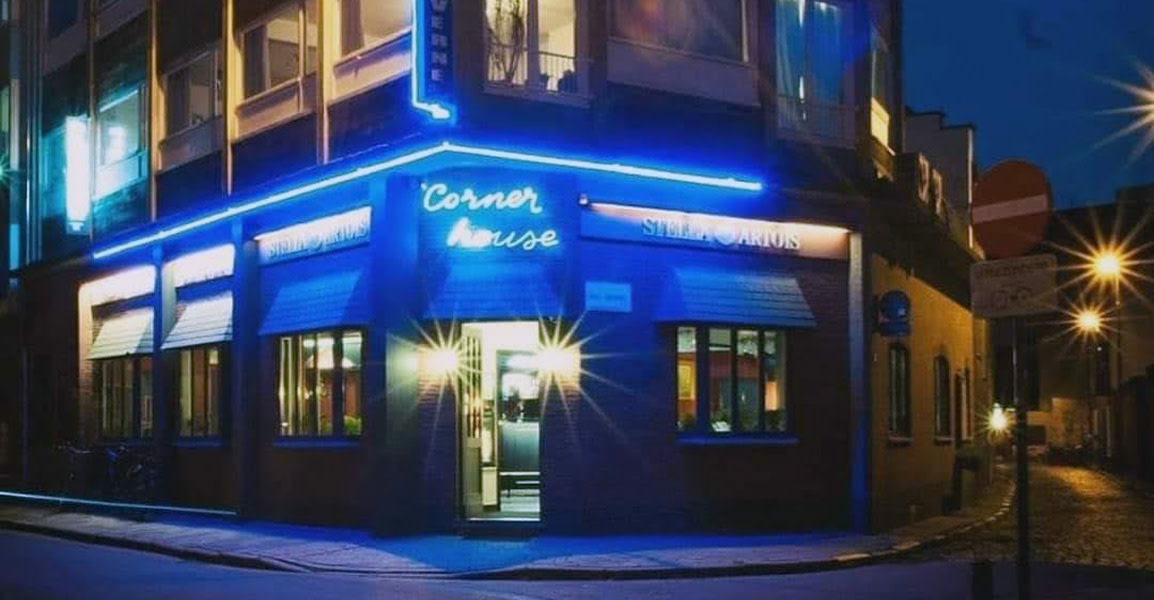 Avondzicht op restaurant Corner House in Hasselt, met blauwe neonverlichting rond de gevel en een uitnodigende entree met twee lichtspots bij de deur.