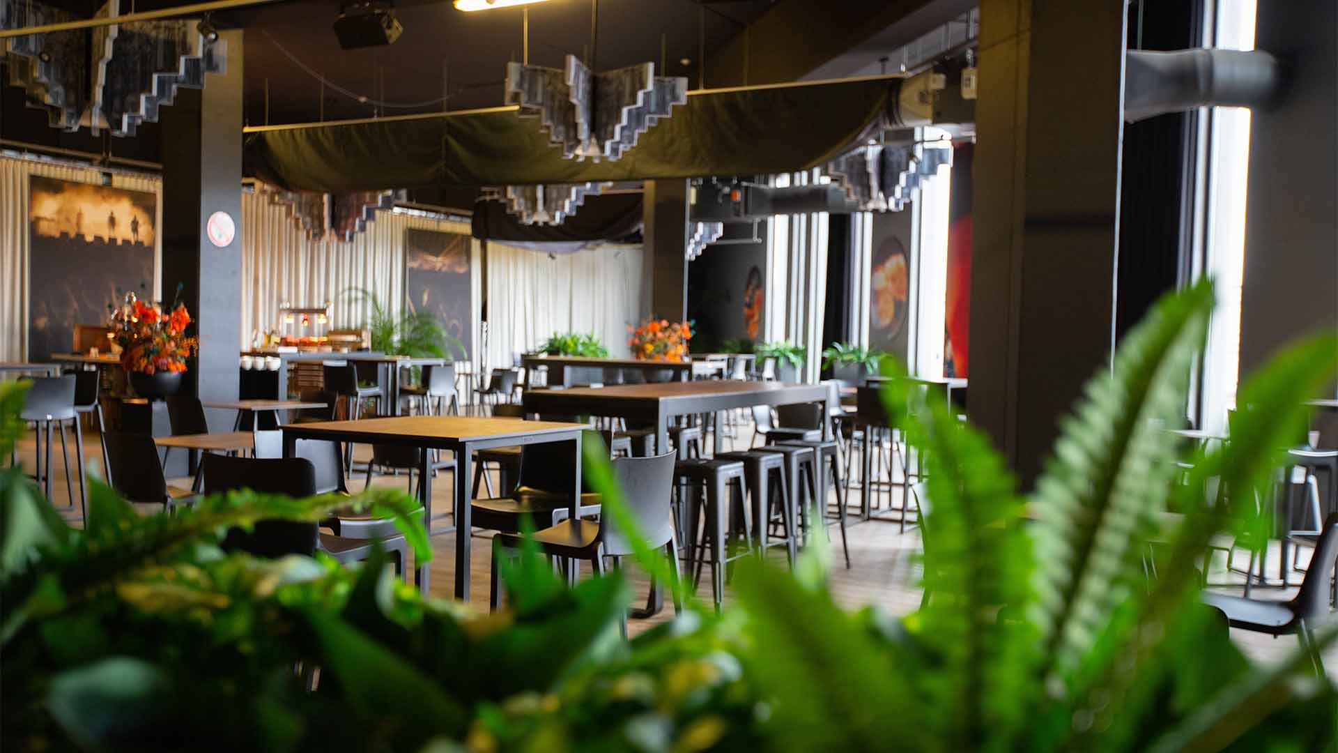 In Lotto Suite 1 staan verschillende hoge tafeltjes opgesteld, sommige met hoge stoelen, andere met krukken. De ruimte is ook gevuld met planten en bloemen.