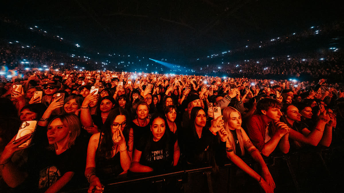 Publiek in een uitverkochte concertzaal dat enthousiast naar het podium kijkt en filmt met smartphones tijdens een liveshow in de Lotto Arena.