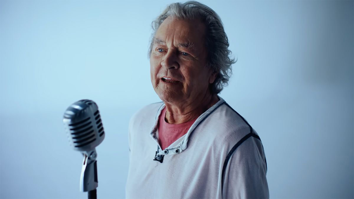 De frontman van Deep Purple tegen een licht blauwe achtergrond voor een microfoon. 