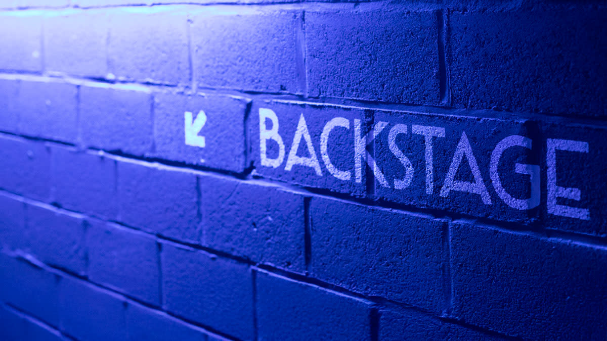 Onze jobcampagne wordt gevisualiseerd door een blauwe muur waarop de vermelding 'Backstage' staat.