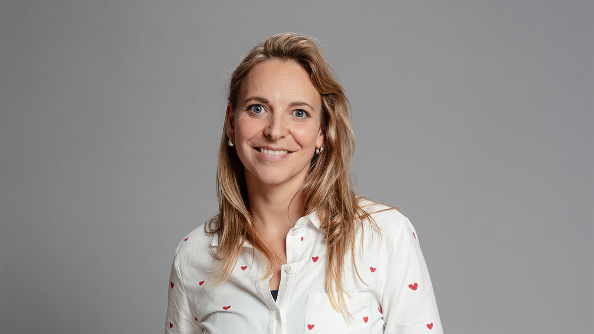 Line Ellegiers poseert voor de camera in een witte blouse met kleine rode hartjes tegen een grijze achtergrond.