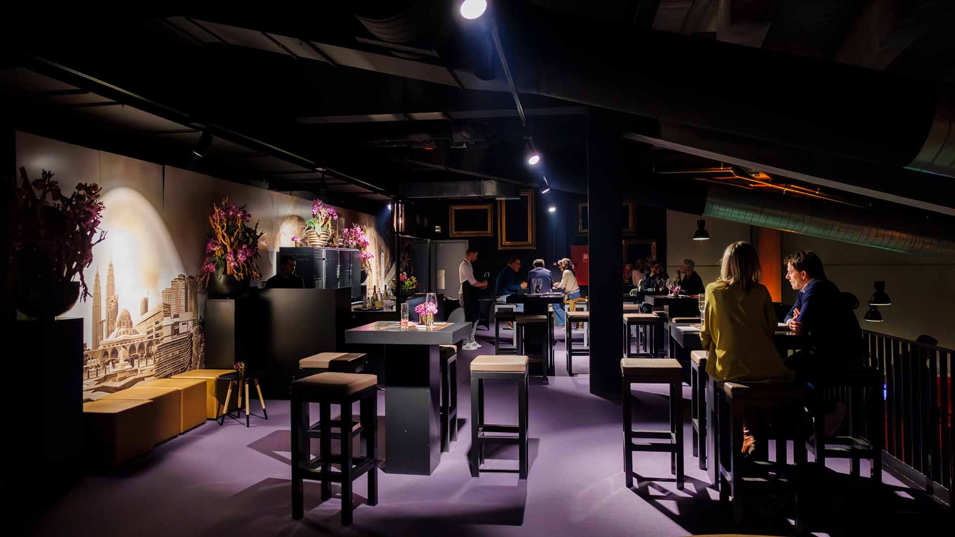 In the loge of Trixxo Theater Hasselt, people are sitting at various tables chatting. The ambient lighting creates a warm and cosy atmosphere.