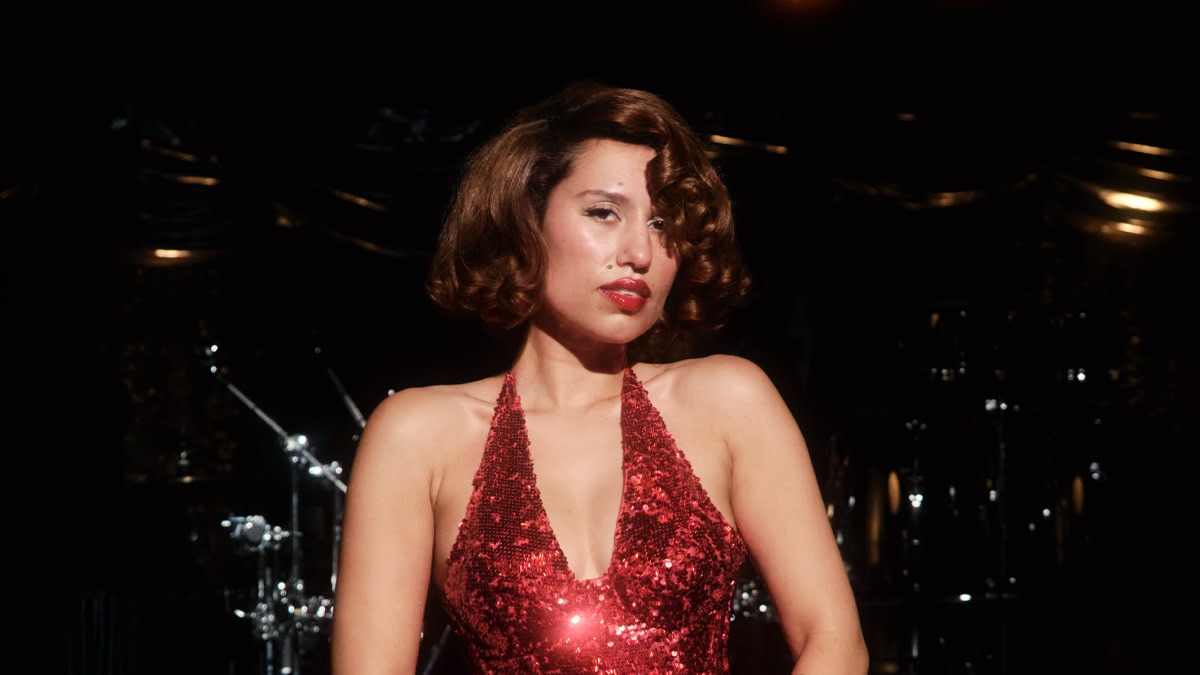 Raye shines in a sparkling red dress against a black background.