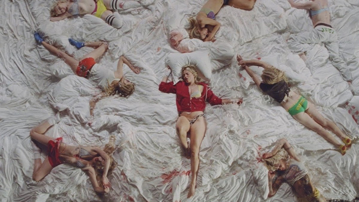 Reneé Rapp ligt languit op een berg witte lakens. Het beeld is een still uit haar videoclip 'Leave Me Alone'.
