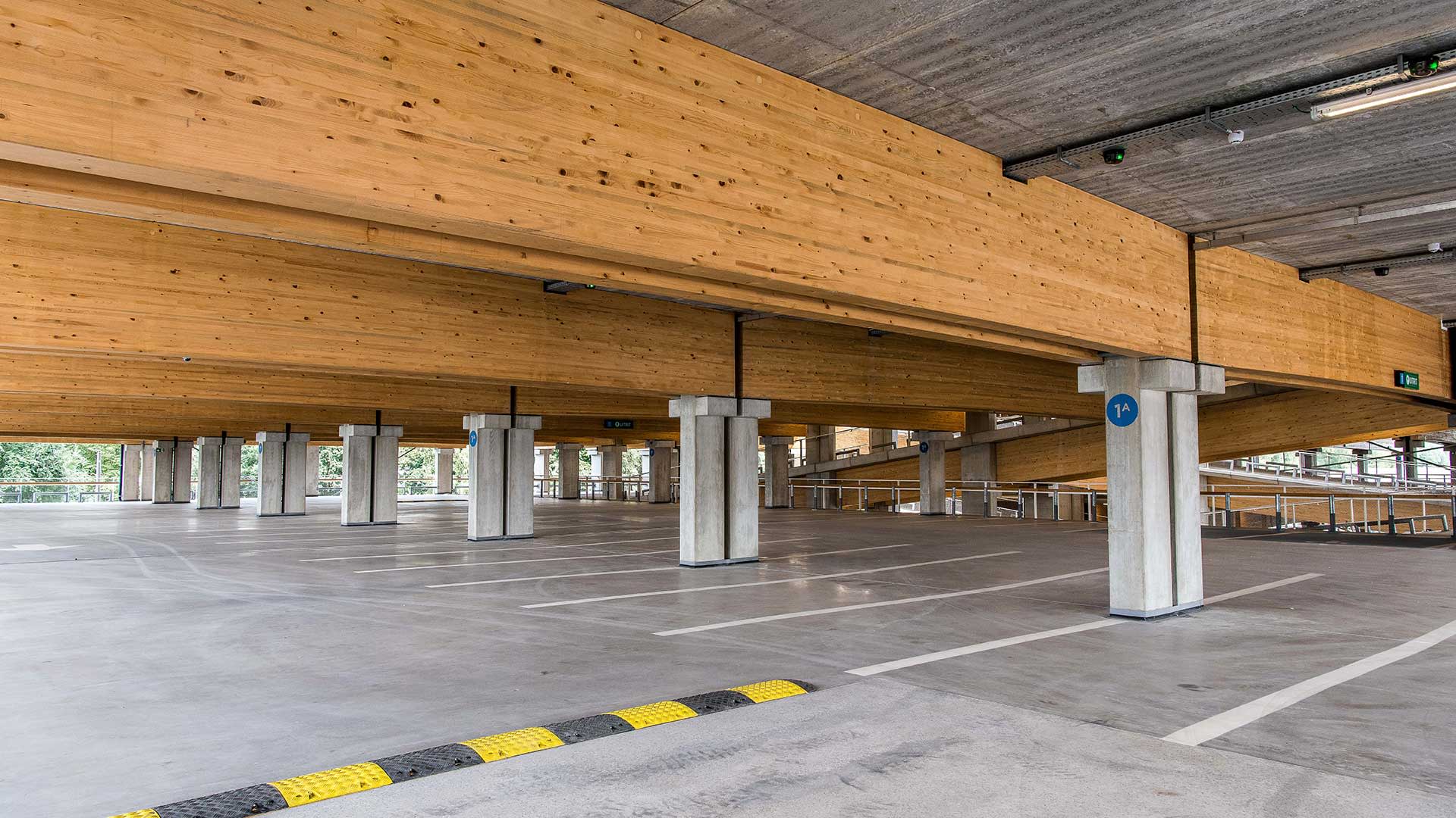 Een grote lege parkeergarage. Aan het plafond hangen zware houten balken.