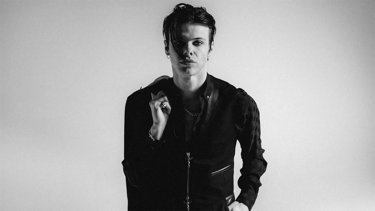 Yungblud kijkt met zijn jas over z'n schouder zelfverzekerd in de camera.