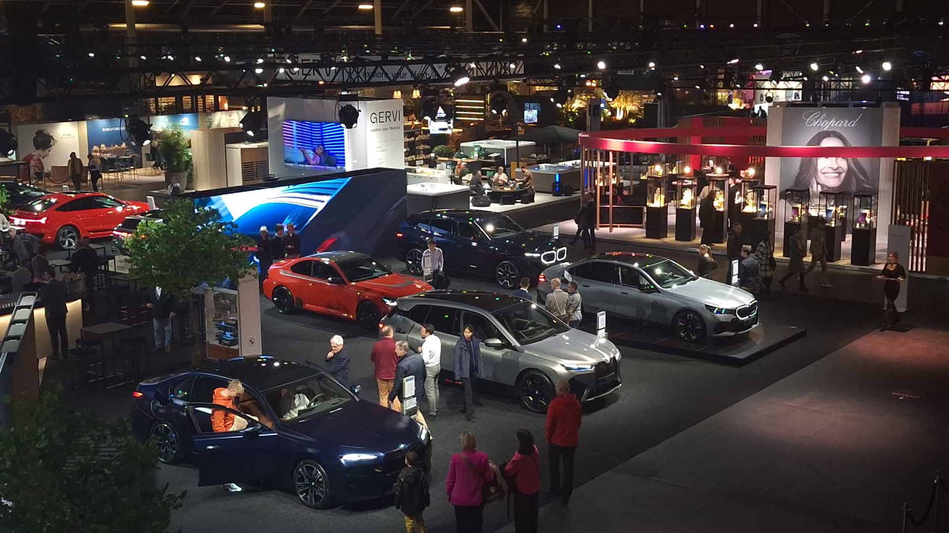 Au salon lifestyle de luxe 'Très Chic', plusieurs voitures de marques prestigieuses sont exposées. Quelques personnes les observent avec intérêt.