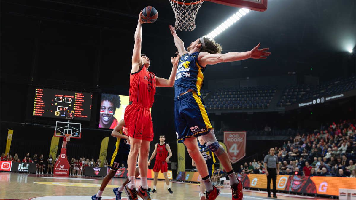 Speler van Windrose Giants Antwerp in rood gaat naar de ring voor een score terwijl een tegenstander van LWD Basket hem probeert te blokkeren tijdens de wedstrijd in de Lotto Arena.