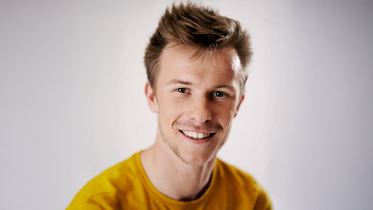 Jasper Heyman in een gele trui en grote glimlach tegen een grijze achtergrond.