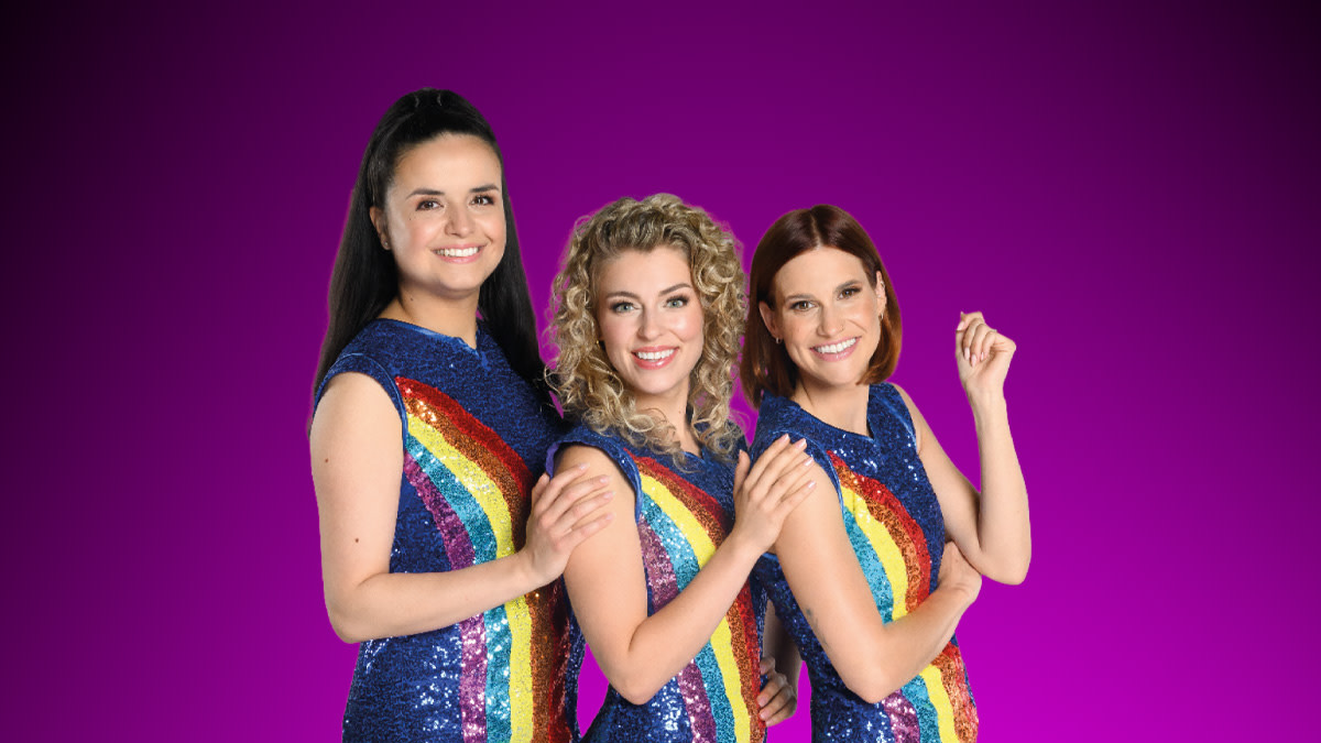 Hanne, Marthe en Julia in hun typische regenboogjurk voor een donkere achtergrond.
