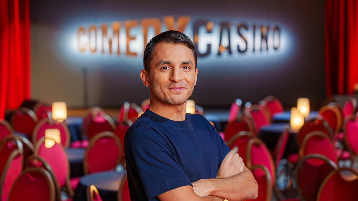 Comedian Mohsin Abbas met de armen over elkaar in een leeg theater met op de achtergrond de woorden 'Comedy Casino'.