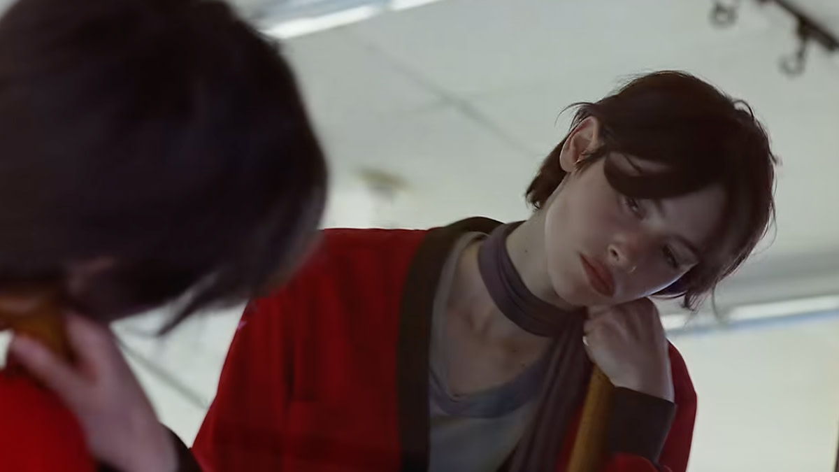 Still uit de videoclip van ‘Look at My Life’ waarin Gracie Abrams peinzend naar haar spiegelbeeld kijkt, gekleed in een rood vest en grijze top.