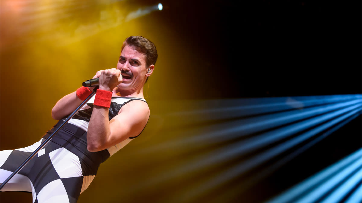 Zanger Michael Kluch van tribute band Queenie op het podium, in iconische Freddie Mercury-outfit, zingend in een microfoon met dramatische belichting en rook op de achtergrond