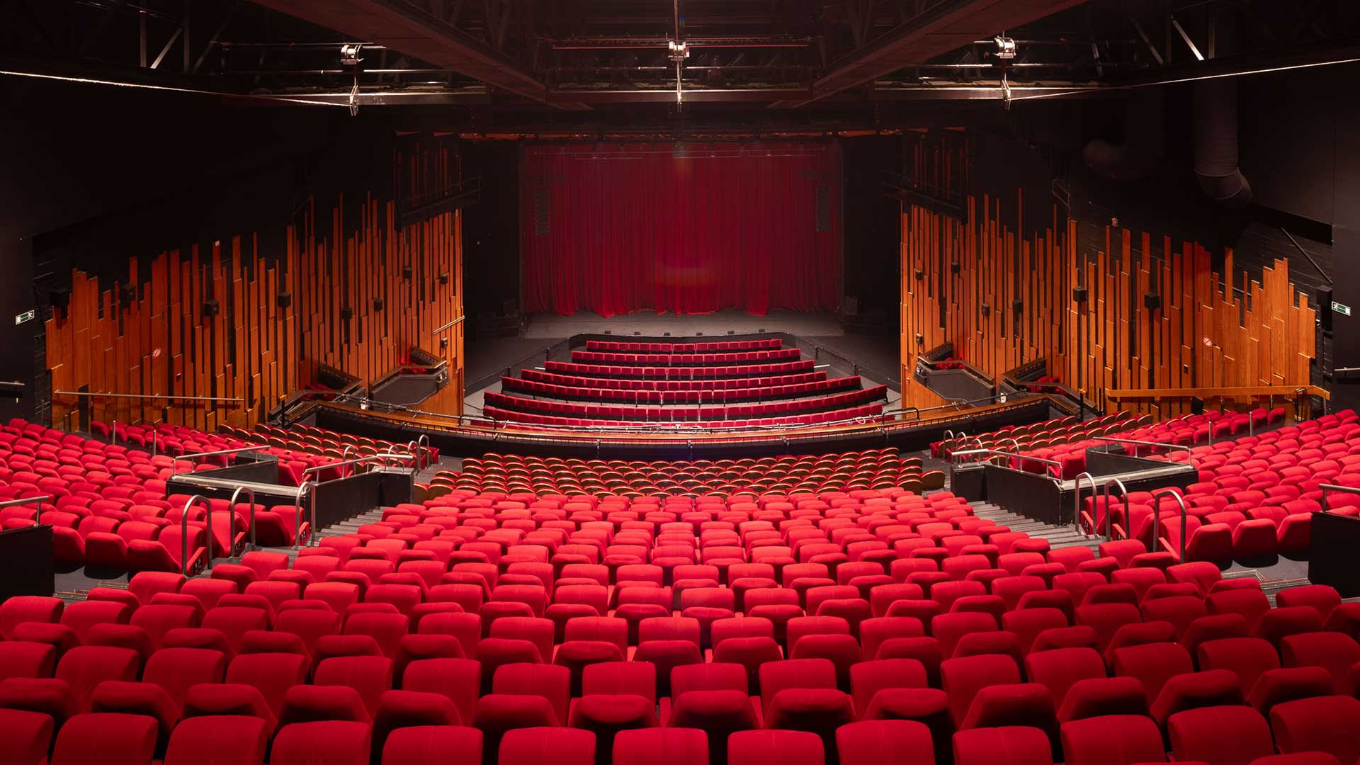 Empty theater hall at Stadsschouwburg Antwerp with red seats, a view of the stage with a closed curtain, and wooden wall panels on both sides.