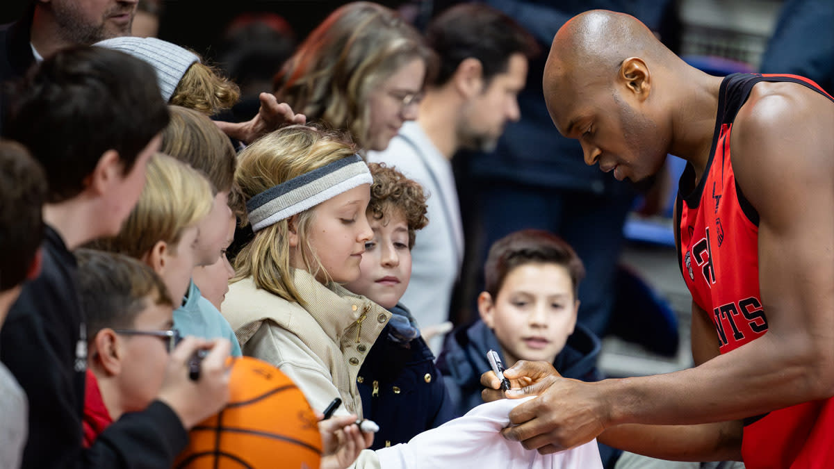 Een speler van de Windrose Giants Antwerp in rode sportoutfit deelt handtekeningen uit aan de kinderen aanwezig op een wedstrijd.