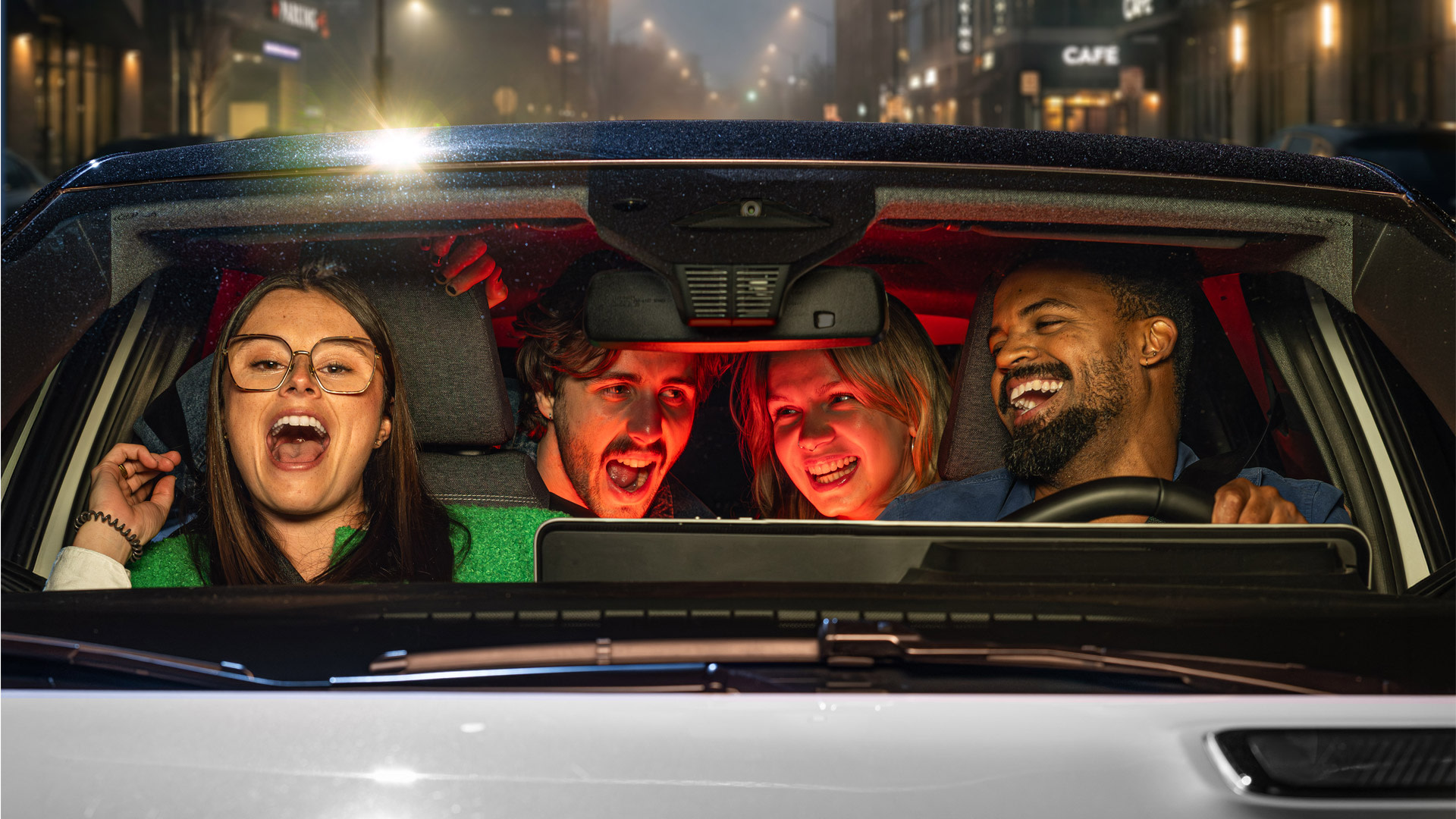 Quatre amis rient et chantent ensemble dans une voiture lors d’un trajet en soirée, illustrant le plaisir et la convivialité du covoiturage.
