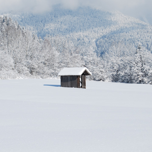 A small log cabin stands in the middle of a snowy field
