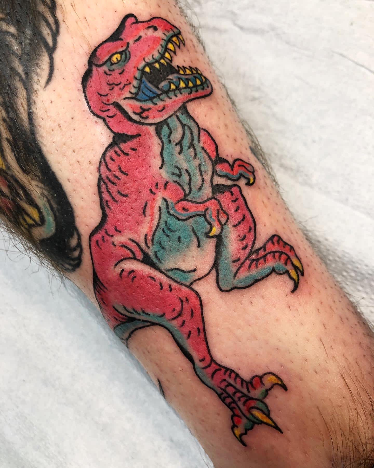Full color portrait of a t-rex coloured in neon pink and blue on the lower calf.