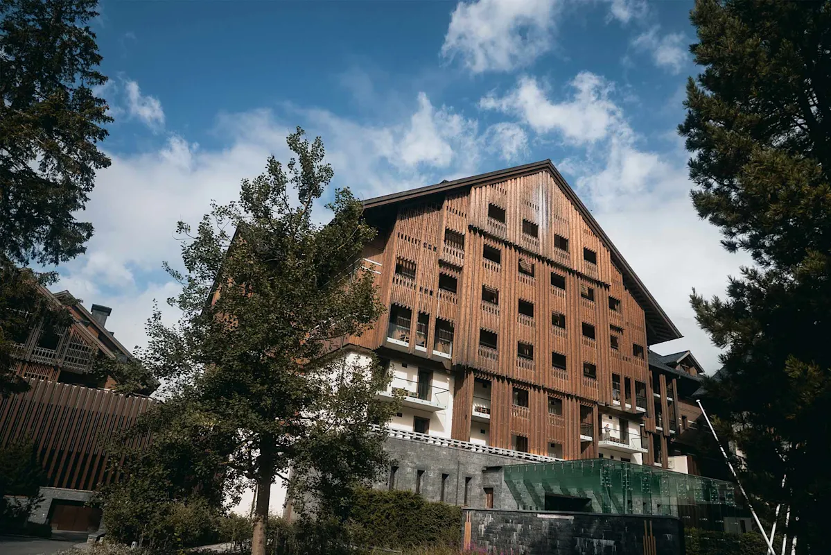 Alpine-style building with balconies among trees under a partly cloudy sky.