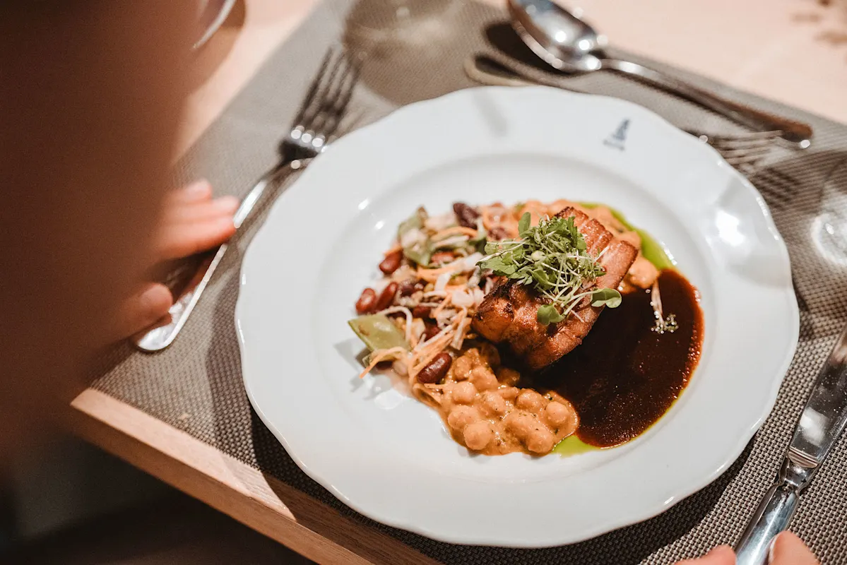 Gourmet-Fleischgericht mit Kichererbsen, Grünzeug, Soße und Besteck.