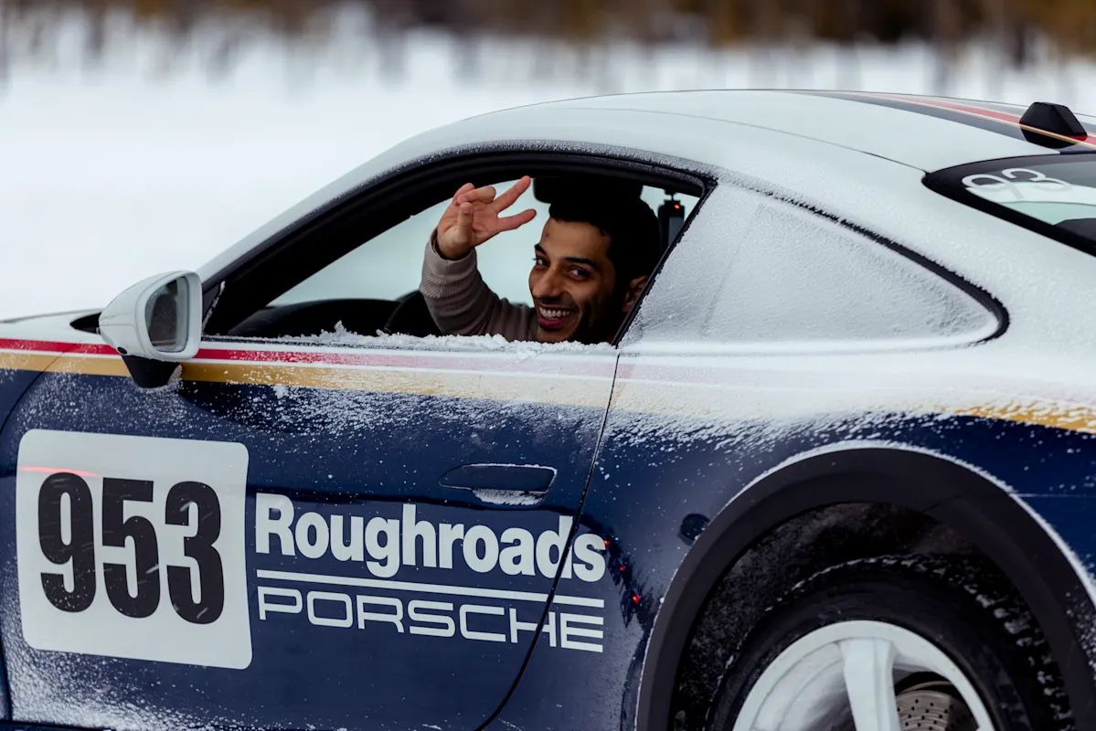 A person flashes a peace sign from a snow-covered Porsche 953 Roughroads.