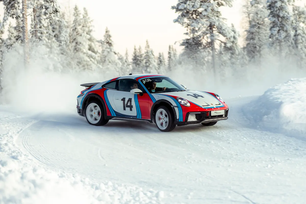Porsche sports car #14 drifts on snowy road among snow-covered trees.