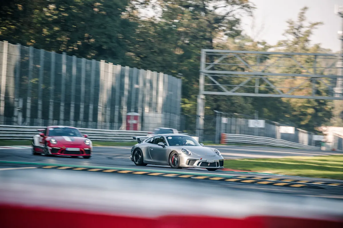 A silver Porsche 911 GT3 drives ahead of a red Porsche 911 GT3 on a race track.