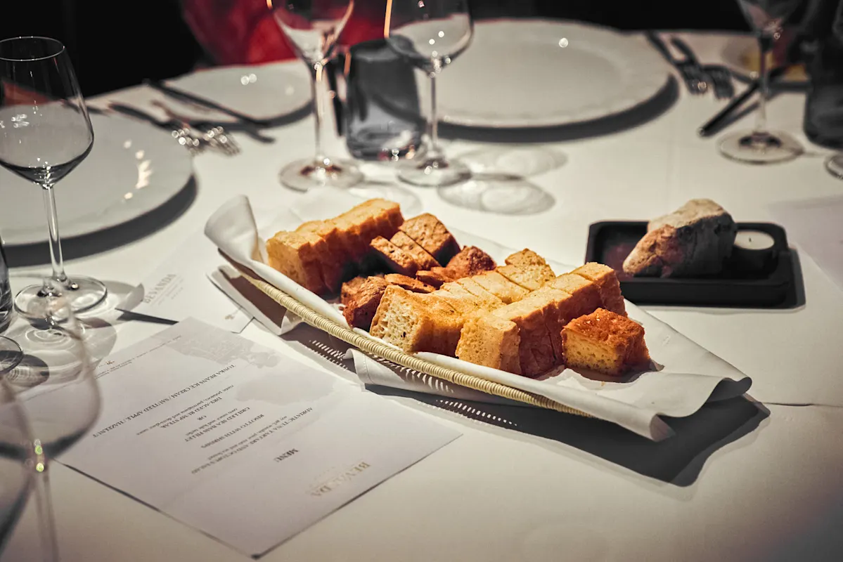 Korb mit Brotstangen, Weingläser und Gedeck auf Tisch.