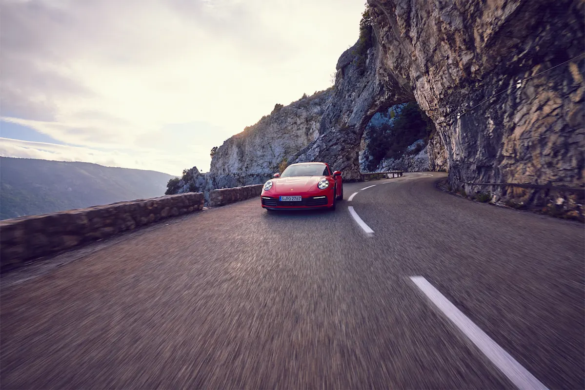 Roter Porsche auf kurviger Bergstraße an Klippe unter Wolken.