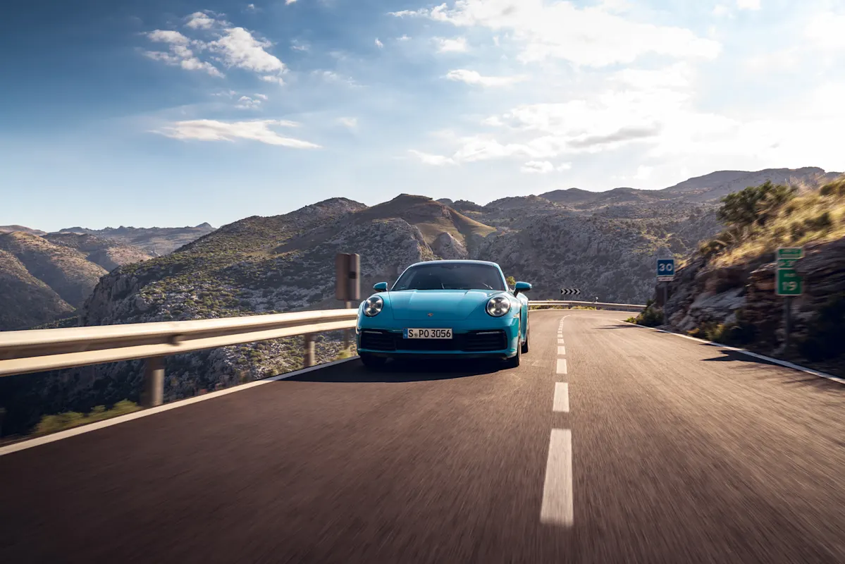 Blauer Porsche auf Bergstraße mit Felsen.