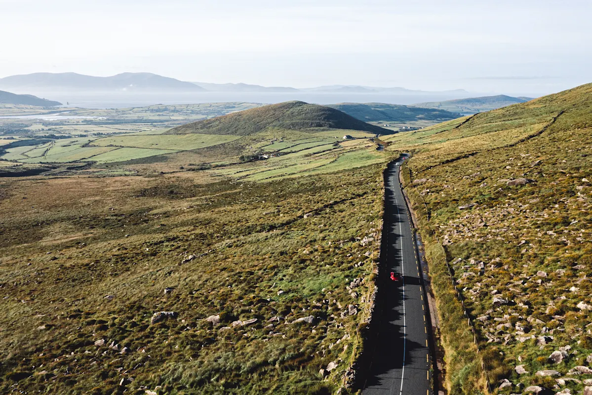 Radfahrer auf kurviger Straße durch Hügel mit Berg- und Wassersicht.