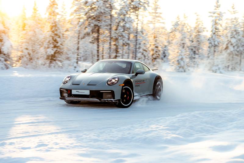 Porsche 911 drifting dynamically across a snowy ice track at sunrise in a winter forest.