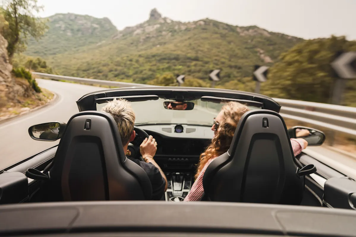 Zwei Fahrer in einem Porsche Cabrio auf einer malerischen Bergstraße.