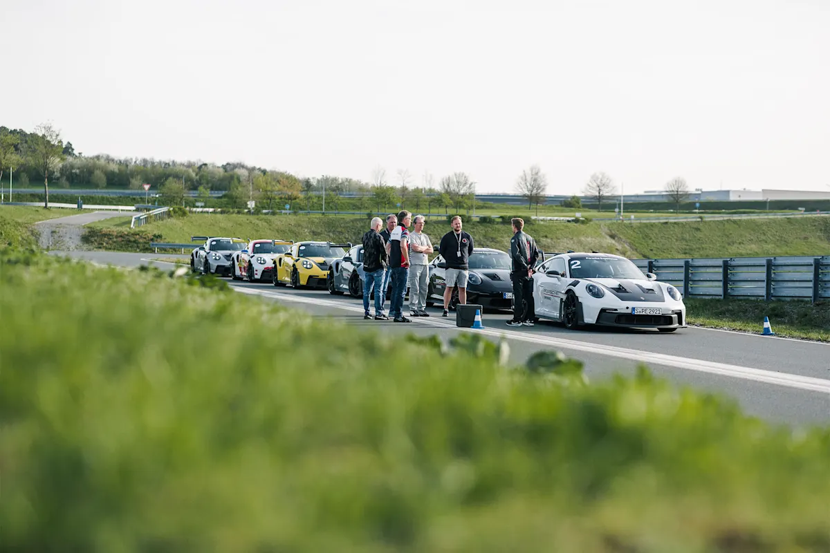 Porsche sports car line on track with spectators, surrounded by nature.