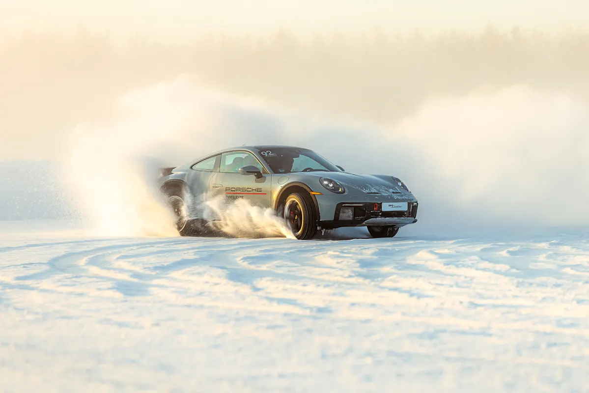 Schwarzer Porsche driftet auf Schneepiste, Schnee wirbelt herum.