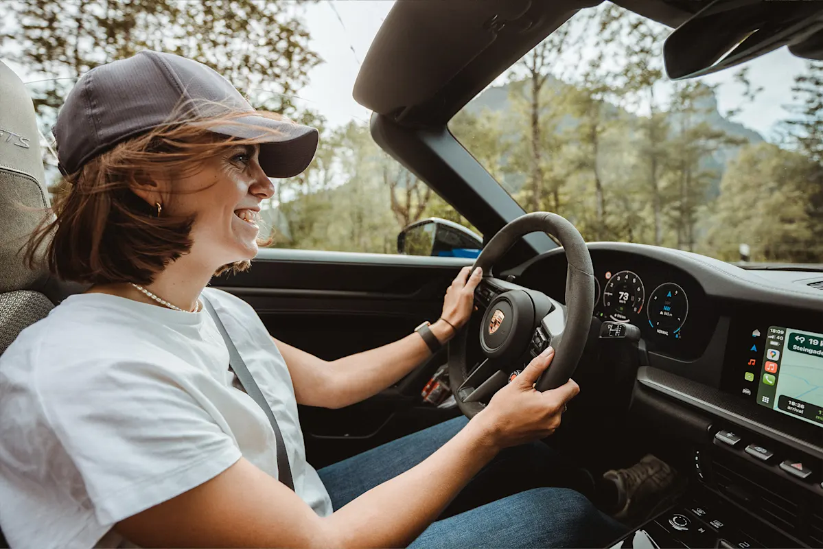 Frau mit Kappe fährt Cabrio durch sonnigen Wald.