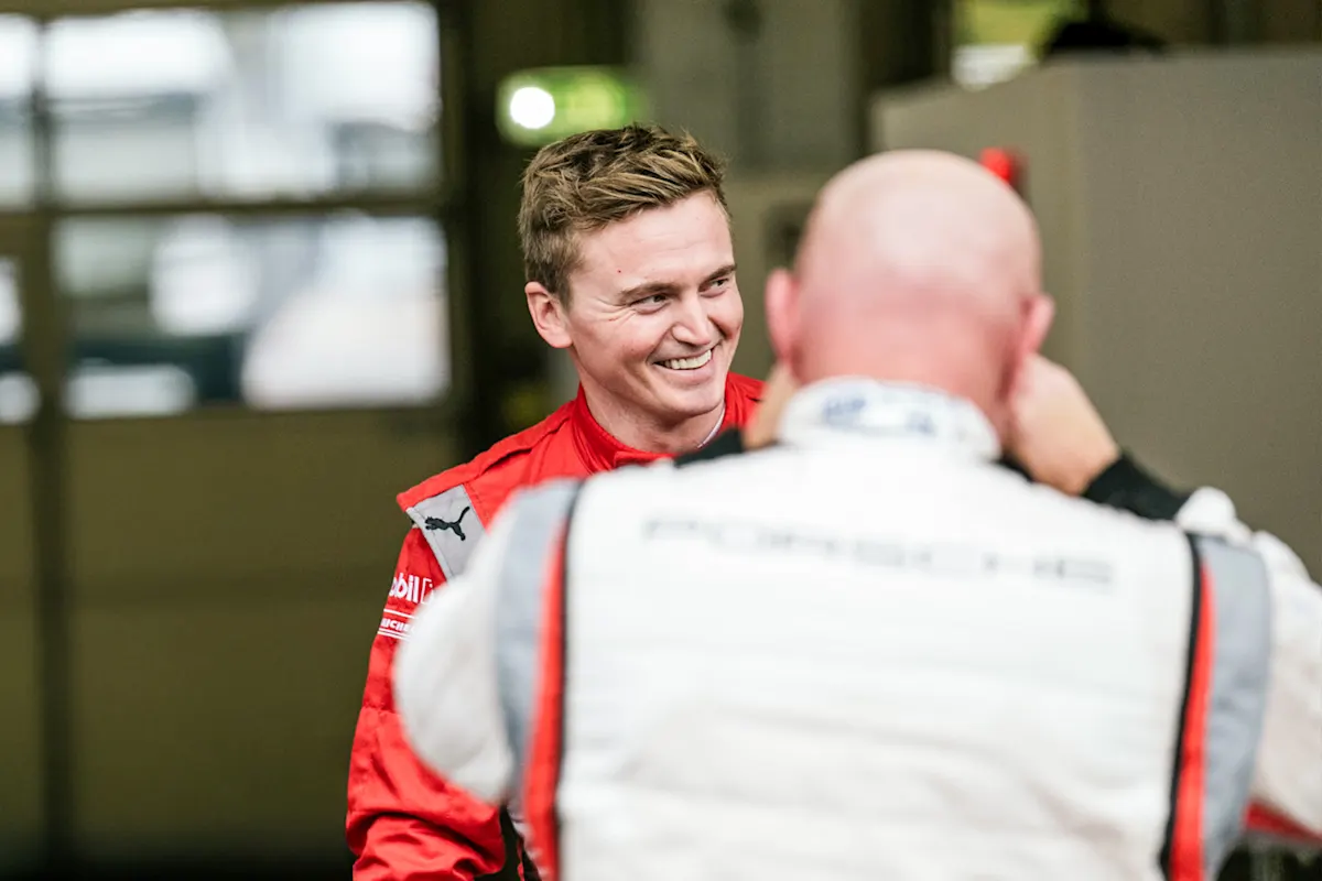 Two men in racing gear, one in red facing the camera, the other in white with his back turned.