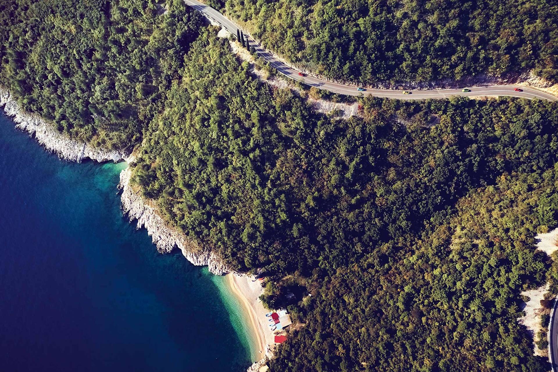 Kurvige Straße an einem Wald, Strand und klarem blauen Wasser.